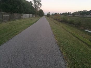 Road amidst agricultural field against sky during sunset