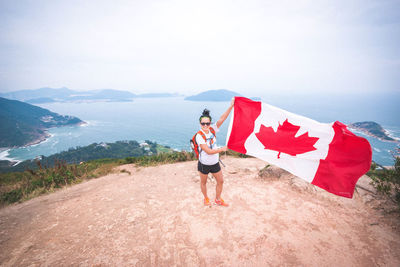 High angle view of excited woman holding canadian flag at dragons back mountain peak against sea