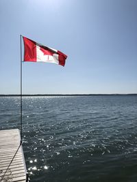 Canadian flag on pier over sea against clear sky