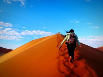 Rear view of man walking on sand dune against blue sky