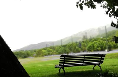 Empty bench on field against clear sky