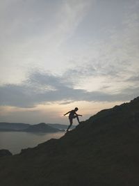 Silhouette person standing on rock against sky during sunset