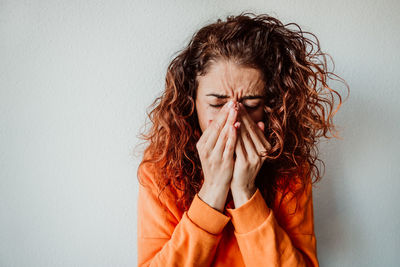 Woman sneezing while standing against wall