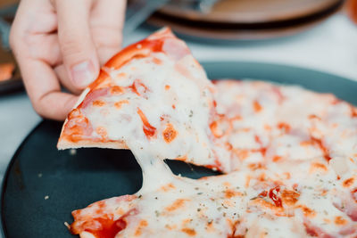 Hand holding very cheesy homemade pizza in cafe.