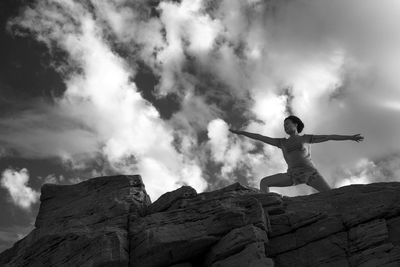 Low angle view of woman stretching with arms outstretched against cloudy sky