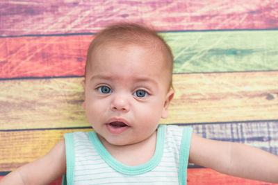 Directly above portrait of cute baby boy lying down on colorful wooden floor