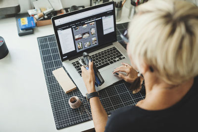 High angle view of industrial designer using laptop while holding product at home office