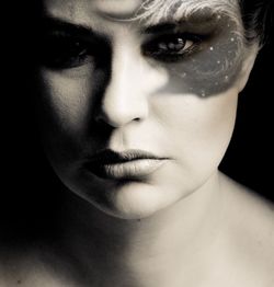 Close-up portrait of serious woman with face paint against black background