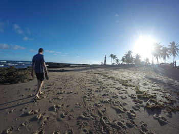 Rear view of man walking on beach against sky