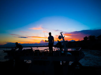Silhouette people standing by sea against sky during sunset