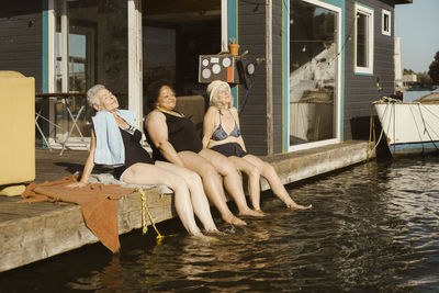 Smiling senior female friends dipping legs in water while relaxing during vacation on houseboat