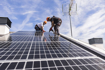 Engineers installing solar panel under sky on sunny day