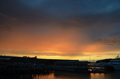 Silhouette buildings by sea against dramatic sky during sunset