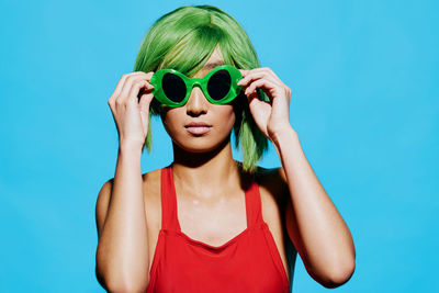 Portrait of woman holding sunglasses against blue background