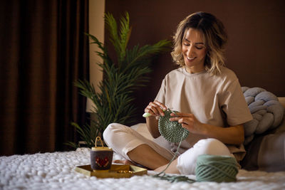 Smiling woman sitting cross-legged doing crocheting at home
