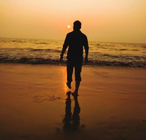 Silhouette man standing on beach against orange sky