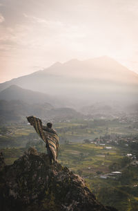 Rear view of man standing on cliff against landscape