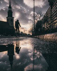 Reflection of silhouette people on puddle in city against sky