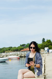 Portrait of young woman wearing sunglasses while standing against lake