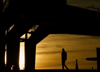 Silhouette man standing on bridge against sky during sunset