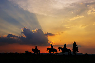 Silhouette people riding horses against sky during sunset