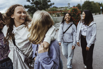 Cheerful female friends talking while walking on footpath