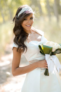 Portrait of smiling bride holding bouquet while standing outdoors