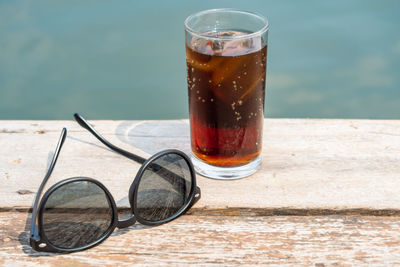 Close-up of cold drink by sunglasses on table outdoors