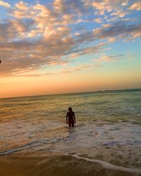 Man standing in sea against sky during sunset