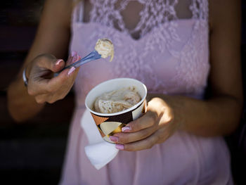 A midsection of woman - hands with spoon eating ice cream