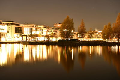 Reflection of illuminated buildings in lake against sky at night