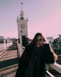 Portrait of woman standing on bridge against clock tower