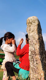 Woman standing on rock against blue sky