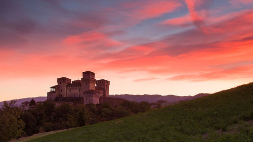 Building on field against sky at sunset