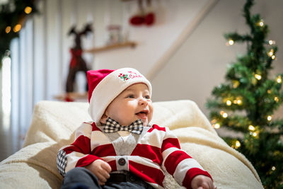 Smiling baby boy on chair against christmas decoration at home