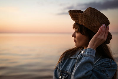 Portrait of a young woman by the sea in a hat at sunset