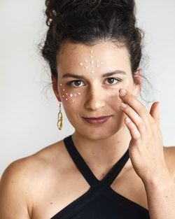 Close-up portrait of woman applying cream on face against white background