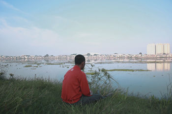 REAR VIEW OF MAN SITTING ON LAND