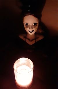 Reflection of woman on illuminated candle in darkroom