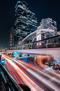 Light trails on rod by illuminated buildings against sky at night