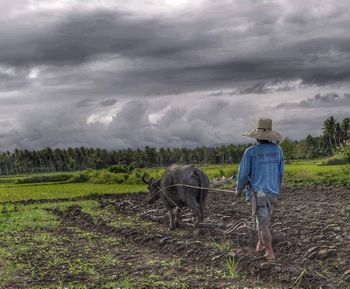 Man standing on field against cloudy sky