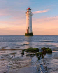 Lighthouse by sea against sky during sunset