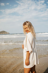 Young woman standing at beach against sky