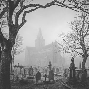 Cemetery by church during foggy weather