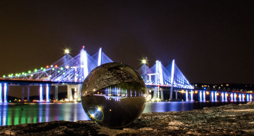 Illuminated bridge over river against sky at night