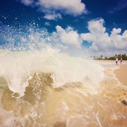 Wave splashing on shore at beach against sky