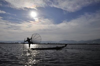 Silhouette man fishing in lake against sky