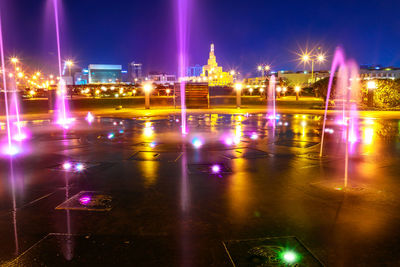 Illuminated city by river against sky at night