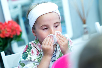 Little girl cleaning face with cotton pads at spa