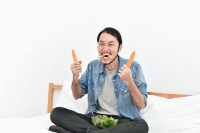 Mid adult man eating salad while sitting on bed against wall at home